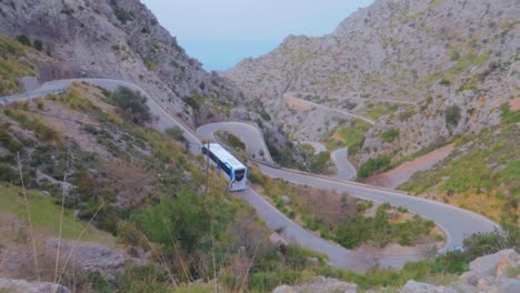 un autobús y un coche se mueven por una estrecha carretera en zigzag en las montañas con bosques frondosos en los inviernos en mallorca, españa