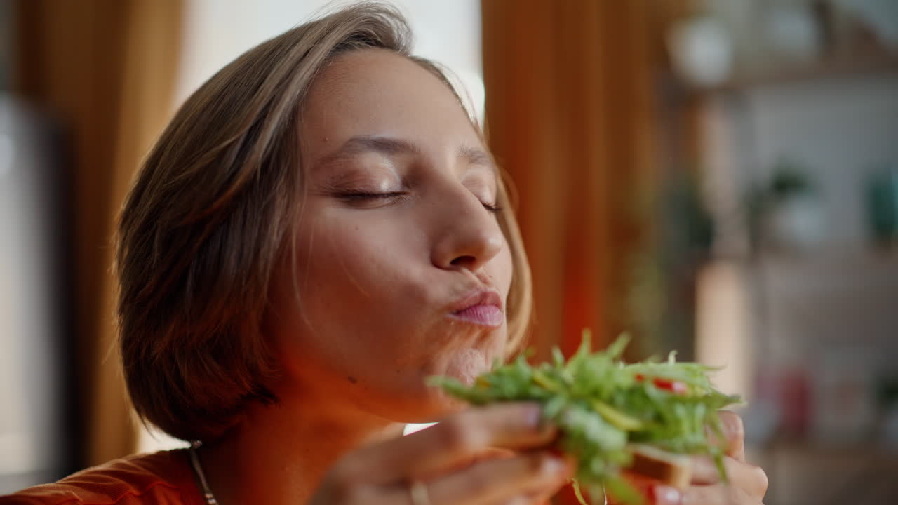 Nahaufnahme einer Frau, die zu Hause in ein Sandwich beißt und ihr Essen genießt. Zufriedene Dame beim Essen