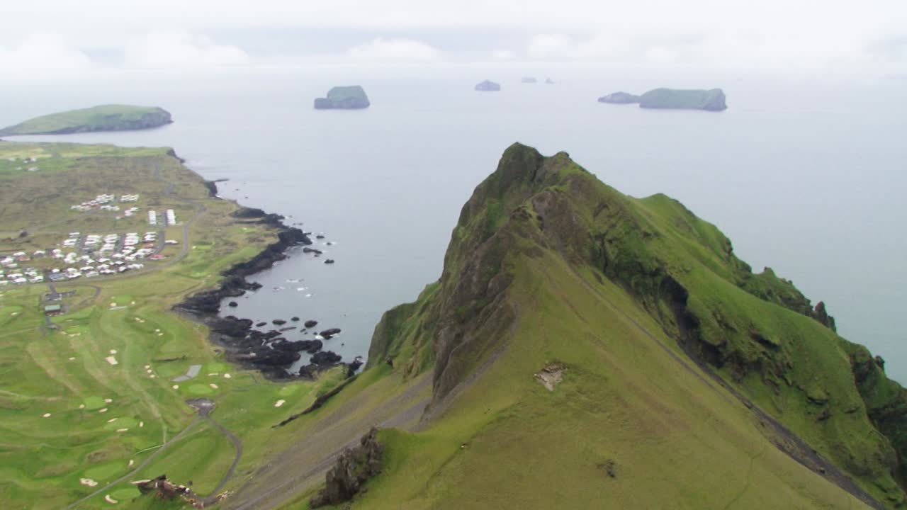 Aerial of green Icelandic cliffs meeting ocean under overcast sky