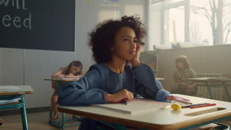 pensive student sitting at school desk in class. female pupil learning science