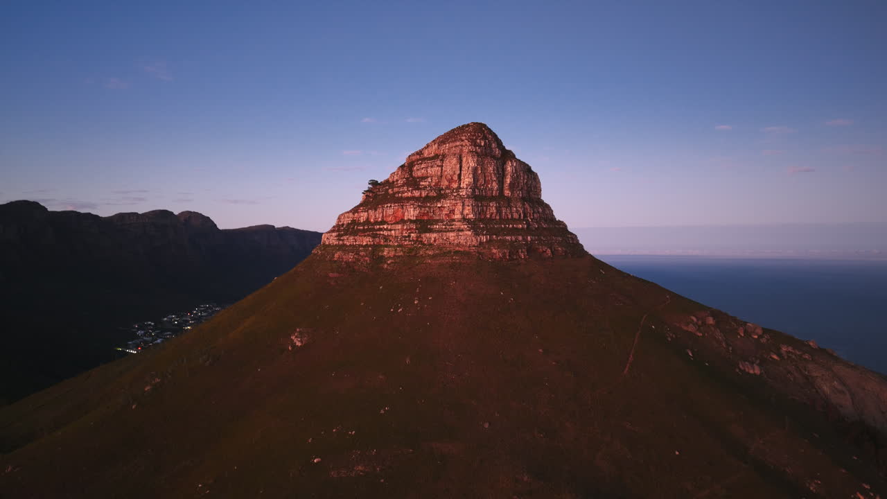 Lion’s Head rises steeply over Cape Town, its rugged slopes bathed in warm evening light, contrasting the green foothills with the vast ocean beyond