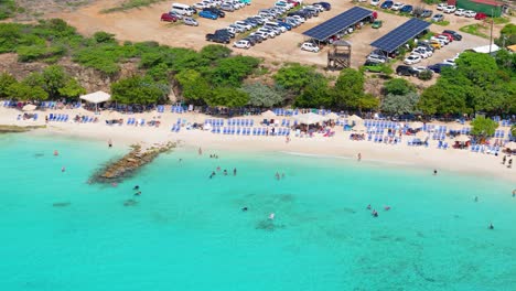 drone trucking pan along playa porto mari passing tourists swimming in turquoise water