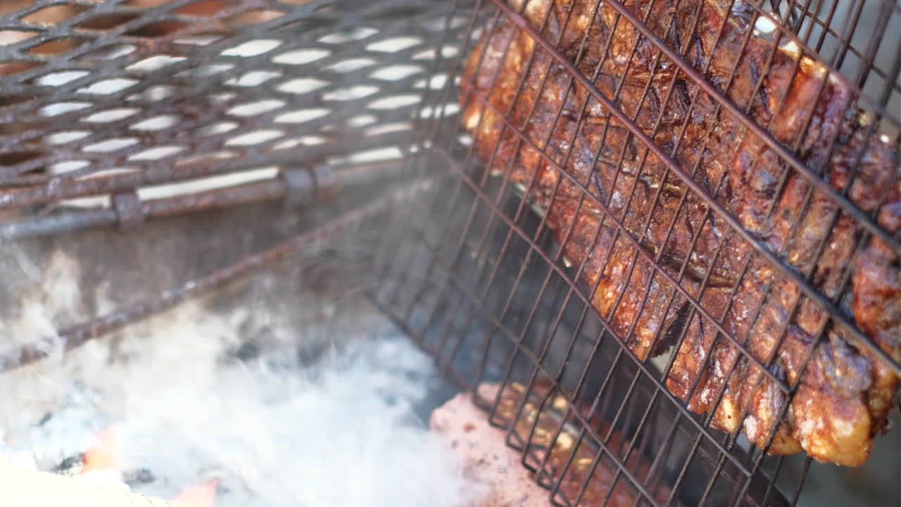 Crispy lamb rib barbecued upright in grid on side of wood fire as fat drips