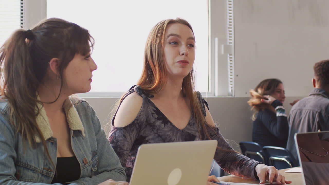 grupo de estudiantes universitarias sentadas en un escritorio usando portátiles colaborando en un proyecto juntos