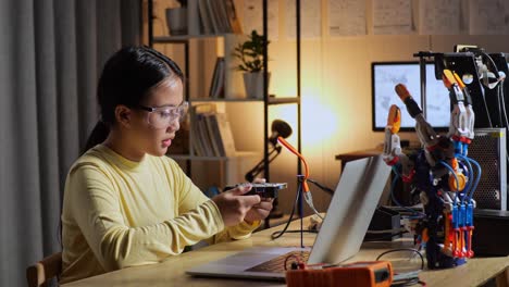 teen asian girl holding and looking at the circuit board while repairing a cyborg hand at home