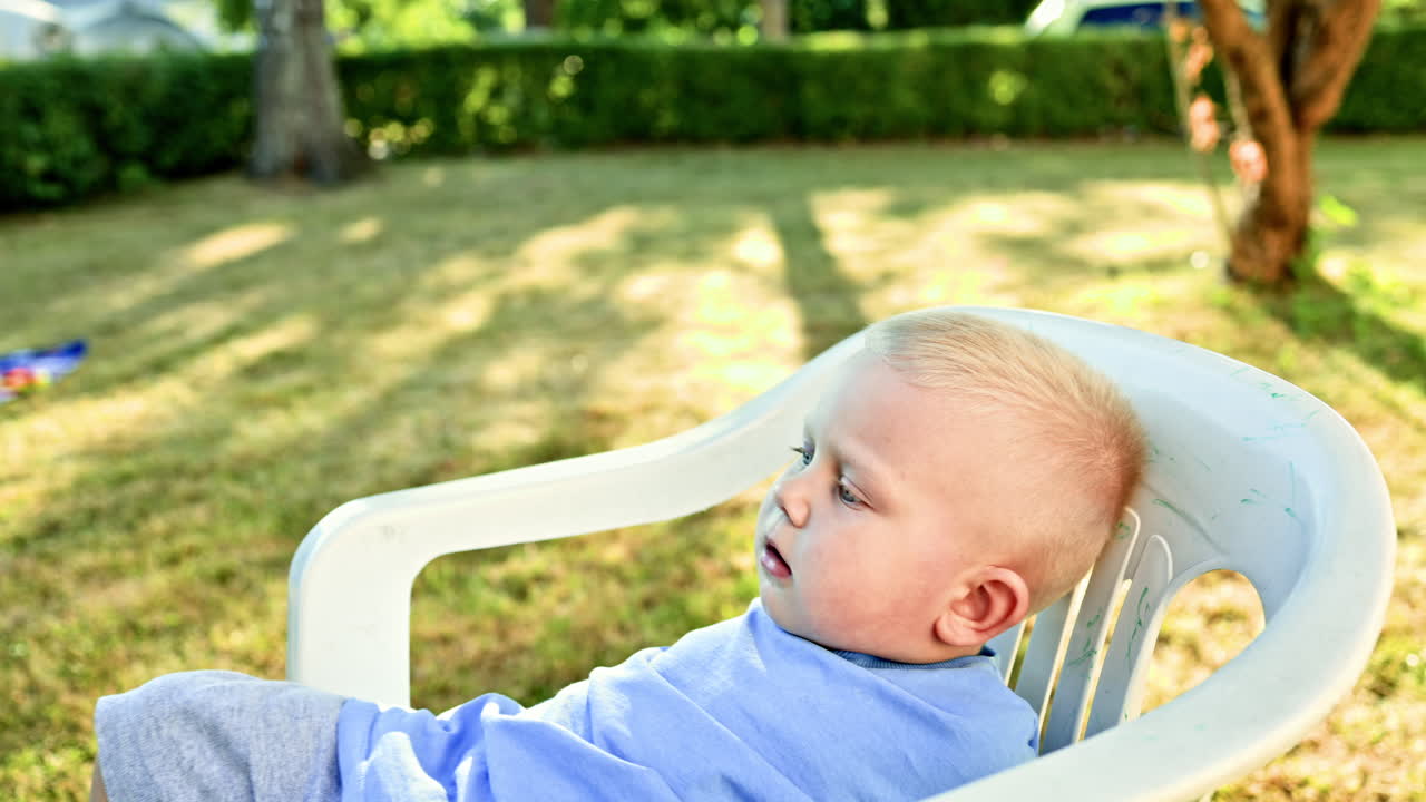 A toddler sits on a plastic chair on the street. Furniture for an outdoor terrace. A child plays in the backyard of a private house