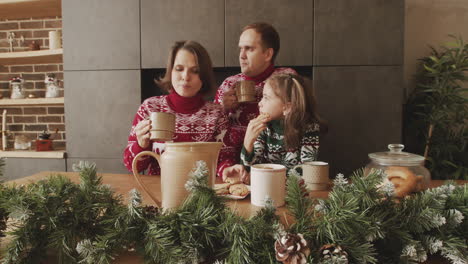 happy family in christmas sweaters drinking and eating cookie on christmas day at home