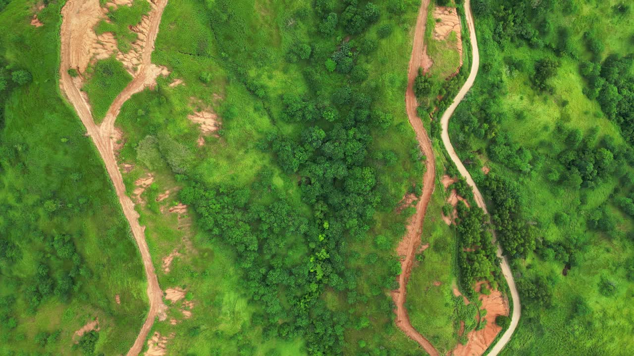 A rotating top view aerial revealing winding dirt roads cutting through green hills and patches of exposed soil of the natural terrain in Quinawan mountain view, Mariveles Bataan, Philippines