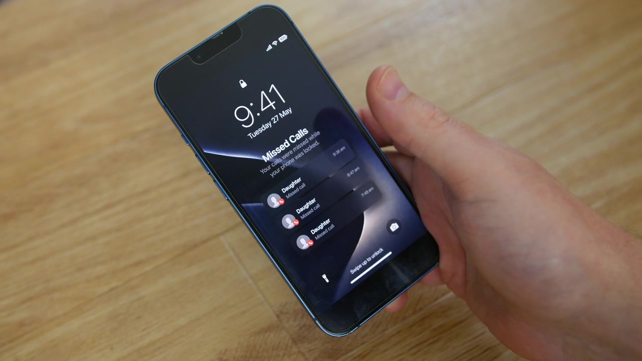 Telefone mostrando chamadas perdidas da Filha repousa sobre uma mesa de madeira enquanto uma mão toca a tela de bloqueio. Vista em close-up de celular, smartphone destaca contato de criança, menina, família e alerta