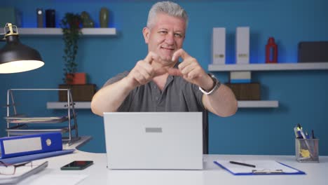 Home-office-worker-man-makes-heart-symbol-looking-at-camera.