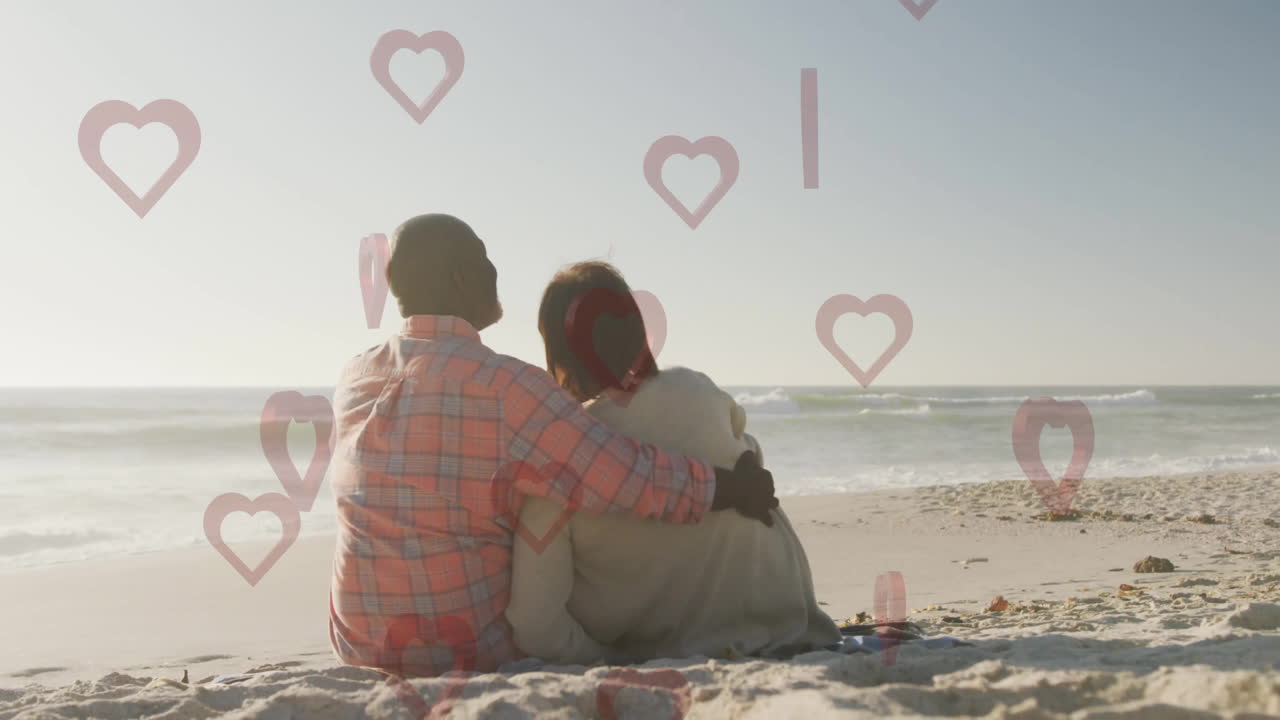 On beach, couple sitting together with heart animation overlaying scene