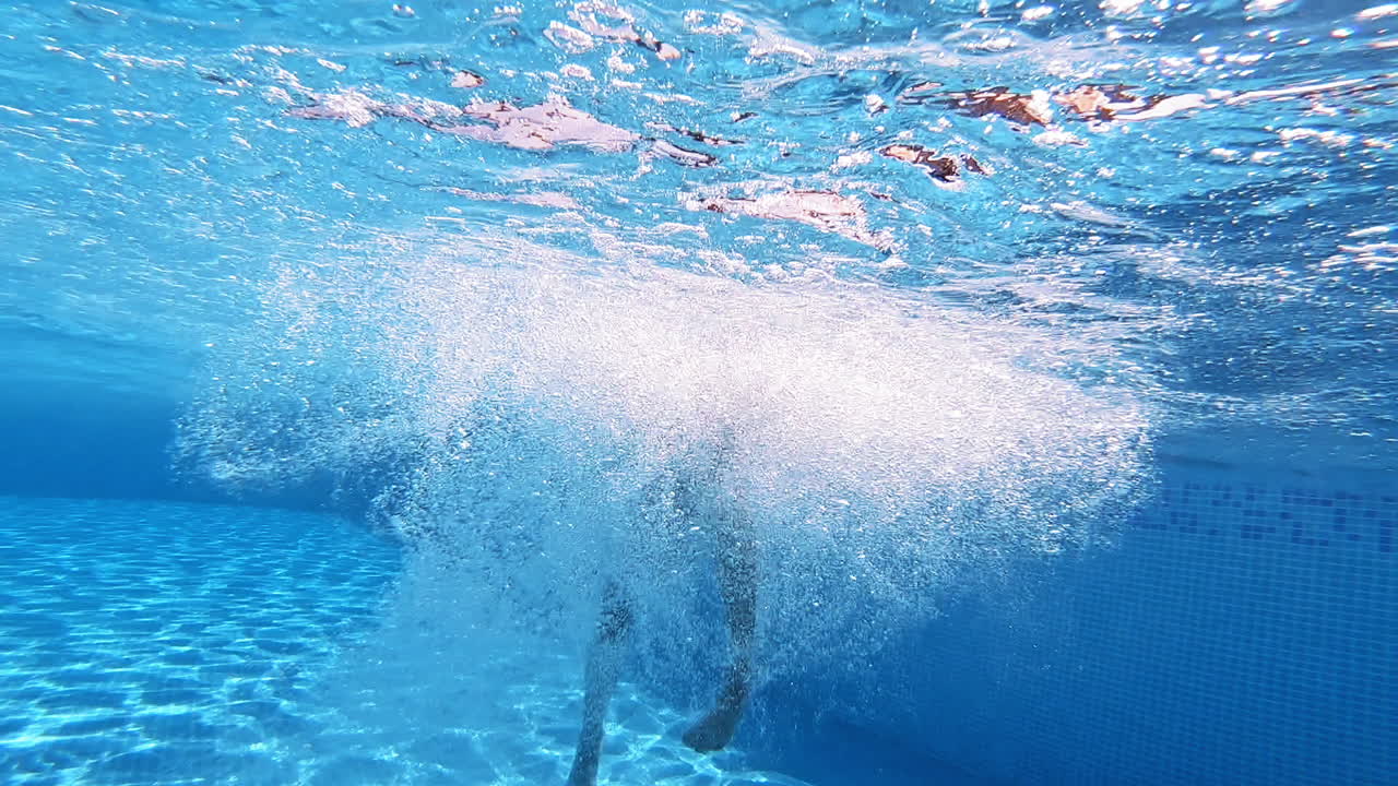 Boy jump into the blue clear water making many bubbles. Young boy jumping underwater into the swimming pool. Underwater camera.