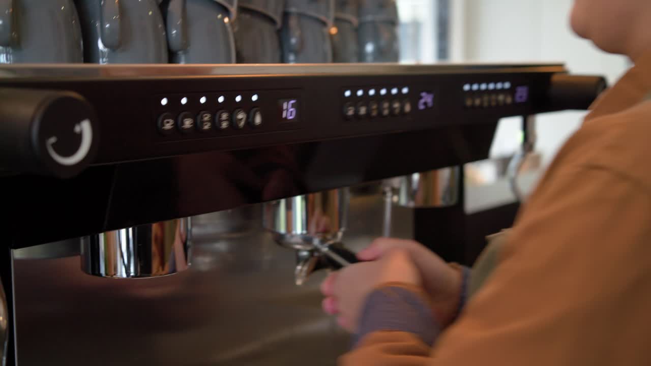 White female barista tamping grounds using tamper at counter, pulling espresso shot to extract brew