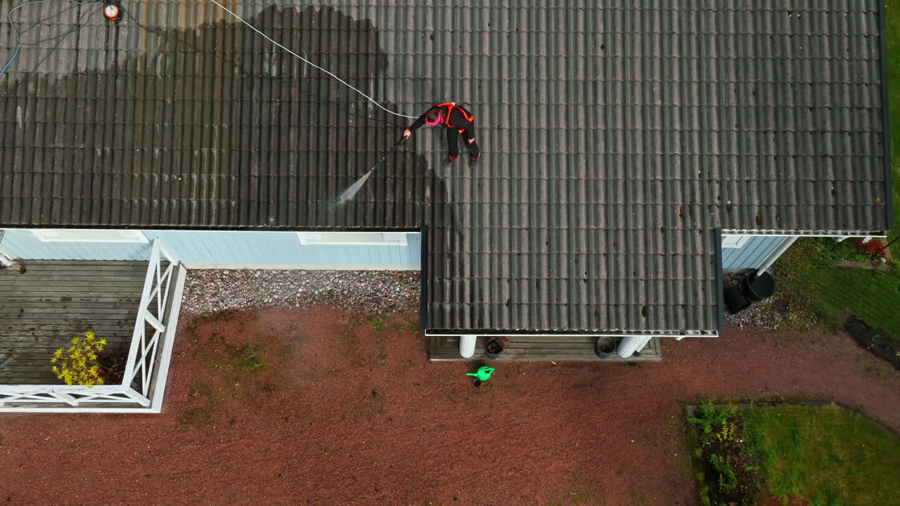 Aerial tilt shot descending above a woman cleaning a house roof, autumn day