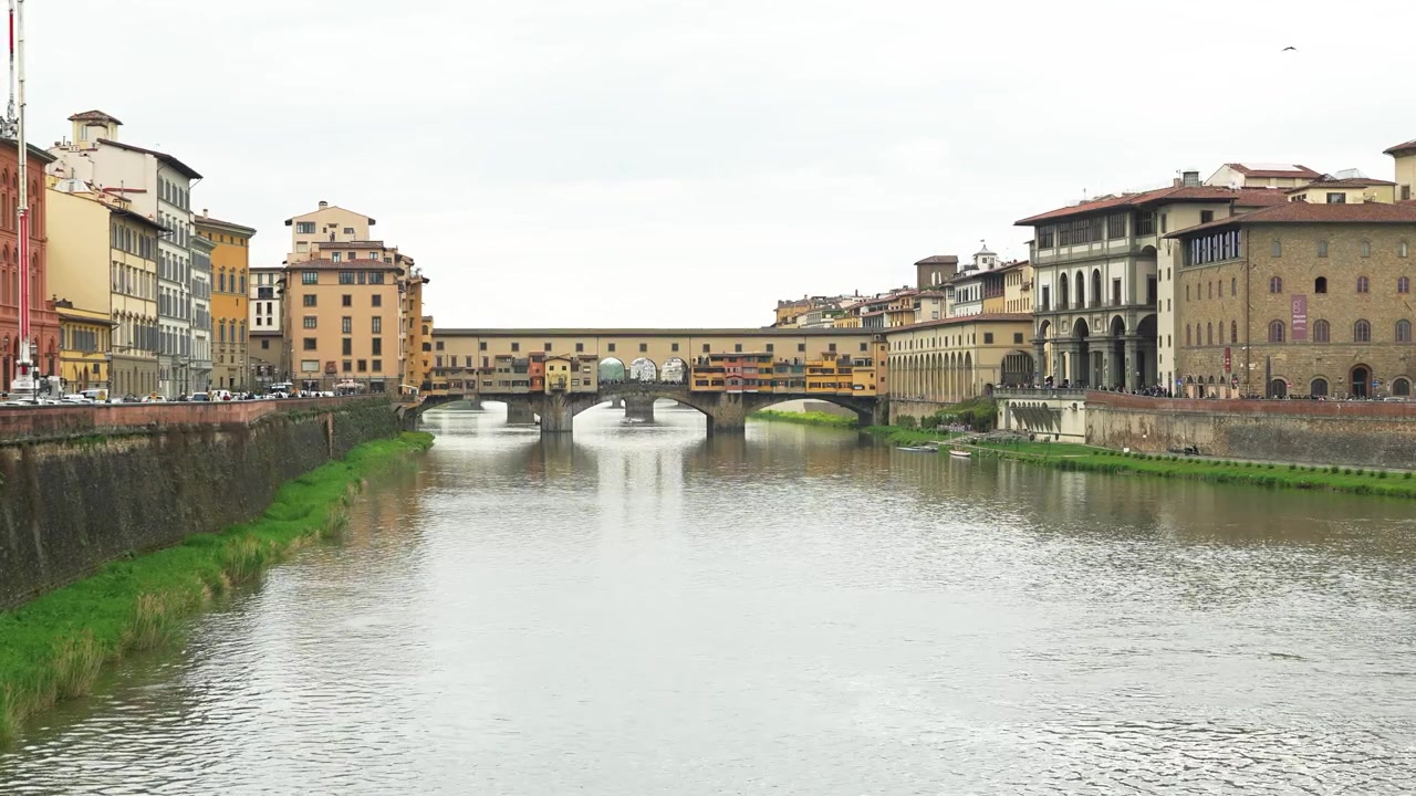 Una ripresa grandangolare cattura lo storico Ponte Vecchio sul tranquillo fiume Arno a Firenze. L'illuminazione naturale diffusa, la vivace architettura lungo il fiume e il sereno paesaggio urbano valorizzano il classico.