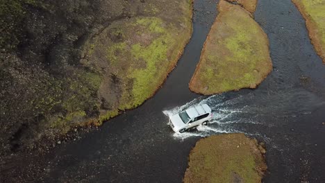 birdseye aerial view of four wheel vehicle in humid landscape of iceland highlands, crossing glacial river water