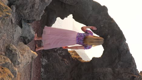 mujer rubia explora el arco de roca escénico en los acantilados de tenerife en la hora dorada, mira hacia el mar