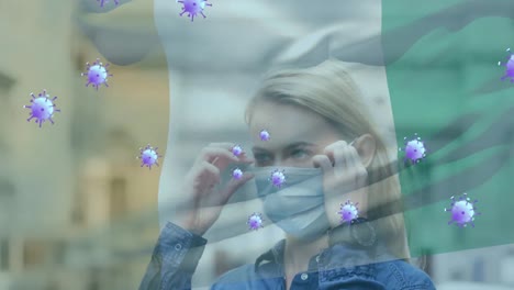 Animation-of-virus-cells-and-flag-of-ivory-coast-over-caucasian-woman-with-face-mask