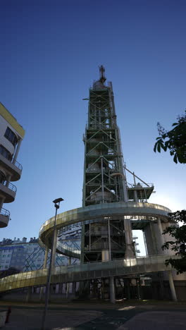 modern architectural structure featuring a tall observation tower with a spiral ramp, surrounded by contemporary buildings under a clear blue sky, showcasing innovative design and urban landscape