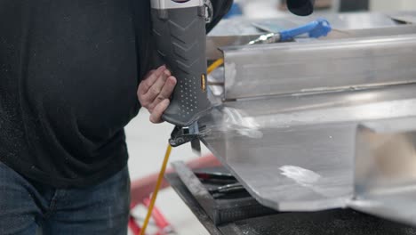 worker's hands using reciprocating saw cutting thick aluminum plate - close-up