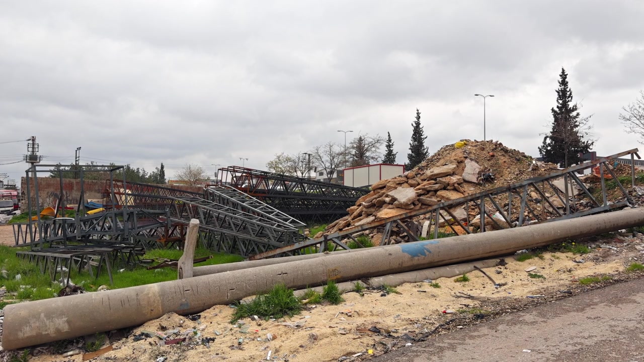 Filmato cinematografico in 4K di una grande struttura a traliccio in acciaio crollata, ammassata sul ciglio della strada con detriti e spazzatura nelle vicinanze. Concetto di degrado urbano, conseguenze di un disastro o demolizione. Cielo coperto.
