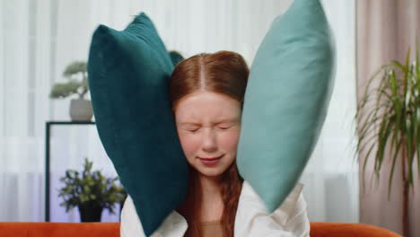 young woman with red hair smiling while holding pillows over her ears