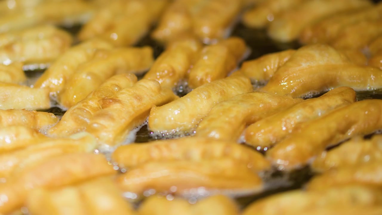 Primo piano di bastoncini di pasta fritta dorati che friggono nell'olio bollente in un mercato.