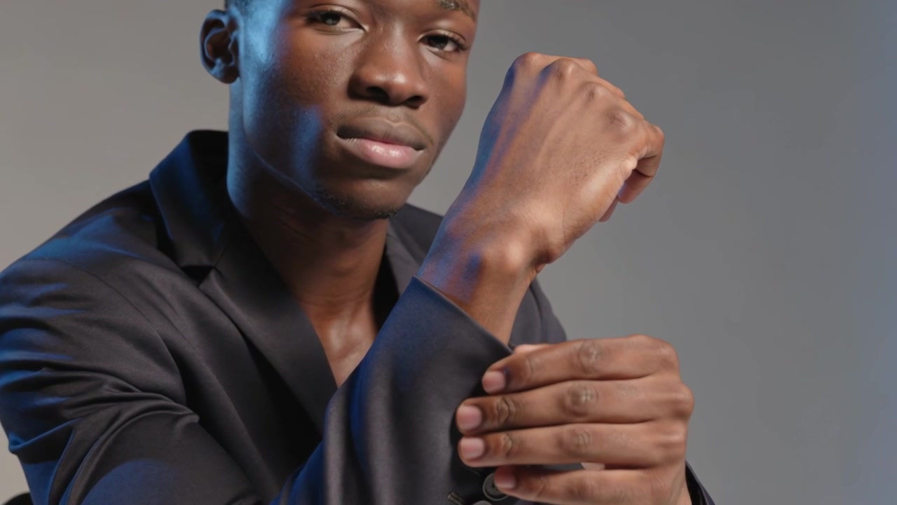 Gazing at camera, male model smoothing right blazer sleeve in studio, revealing patterned cuff