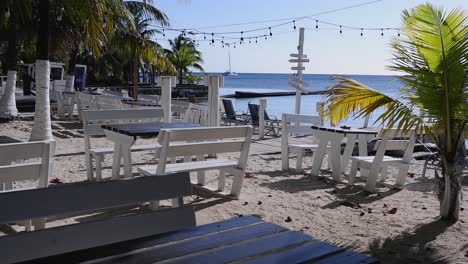 Panorámica-Sobre-Mesas-Y-Bancos-De-Madera-En-Un-Restaurante-De-Playa-En-Roatán,-HND.