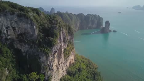 an aerial drone shot of cliffs and mountains by the sea and ocean water in portugal while small boats and yachts, motorboats are riding on the blue water