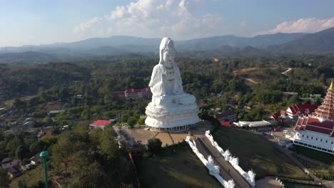 aerial of wat huay pla kang giant white big statue and pagoda temple with mountains and landspace in chiang rai, thailand