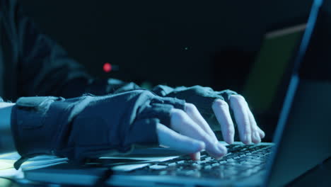 closeup shot of human hands in fingerless gloves typing on grey keyboard in dark room while hacking or coding at night