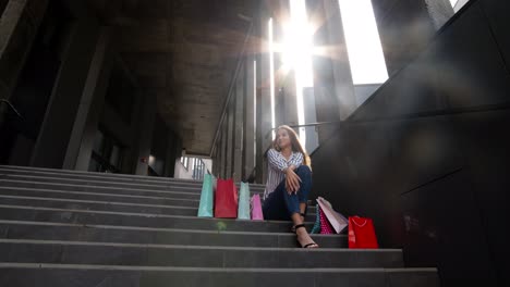 teenager smiling girl with shopping bags sitting on stairs near shopping mall. black friday sale