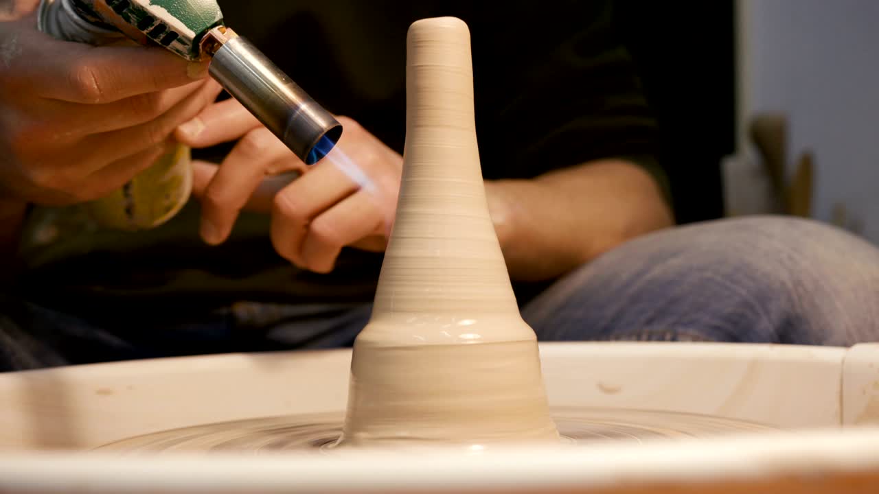 Clay on the potter's wheel and gas burner in hands