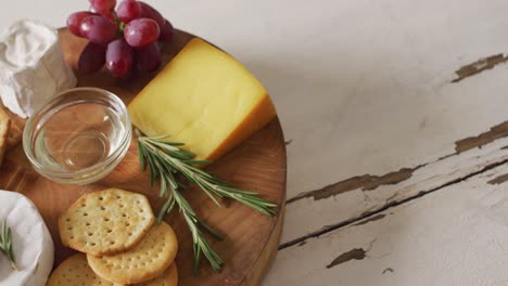 video of cheese, biscuits, grapes and rosemary on wooden board and rustic table top with copy space