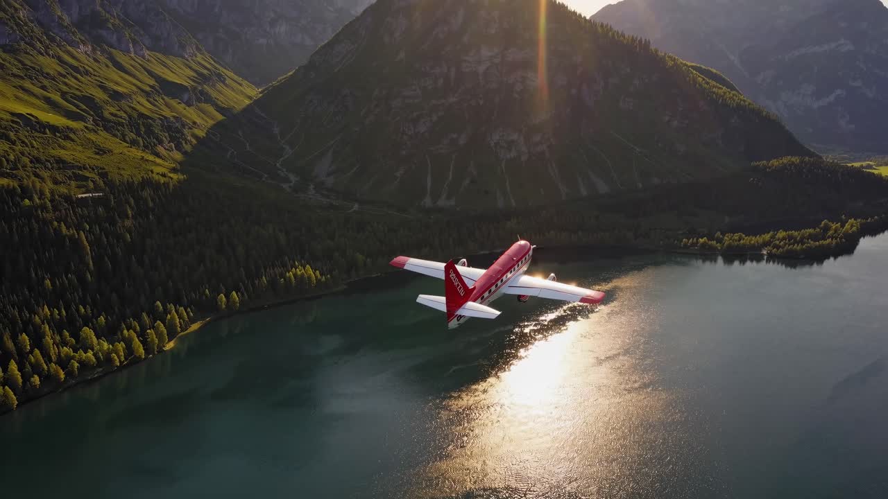 perspectiva aérea revelando un avión rojo y blanco deslizándose sobre un tranquilo lago de montaña, reflejando el resplandor dorado del atardecer a través del prístino paisaje alpino