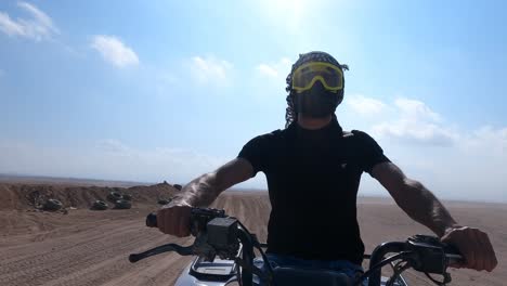 arabian man riding atv driving fast in egyptian desert wearing protective gear of sand goggles, dust face mask and shemagh