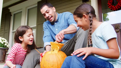 padre e hijas tallando calabaza de halloween en los escalones de la casa