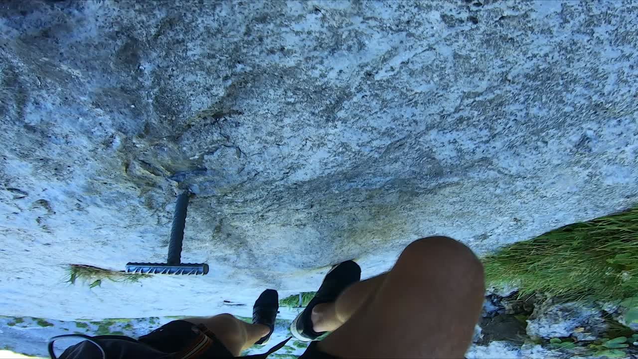 toma de pov de un hombre fuerte que sube por la empinada ladera de una montaña con solo pequeños alfileres de metal como escalones de su escalera
