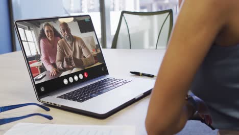 African-american-woman-using-laptop-for-video-call,-with-diverse-business-colleagues-on-screen