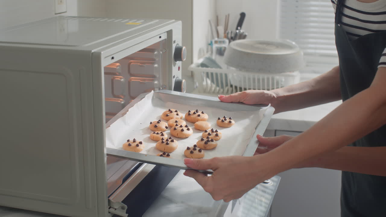 Unrecognizable Mother and Daughter Putting Baking Form with Cookies in Oven