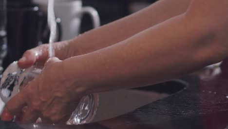 Manos-De-Mujer-Enjuagando-Un-Vaso-De-Vidrio-Bajo-El-Grifo-De-La-Cocina-En-Casa-A-Cámara-Lenta