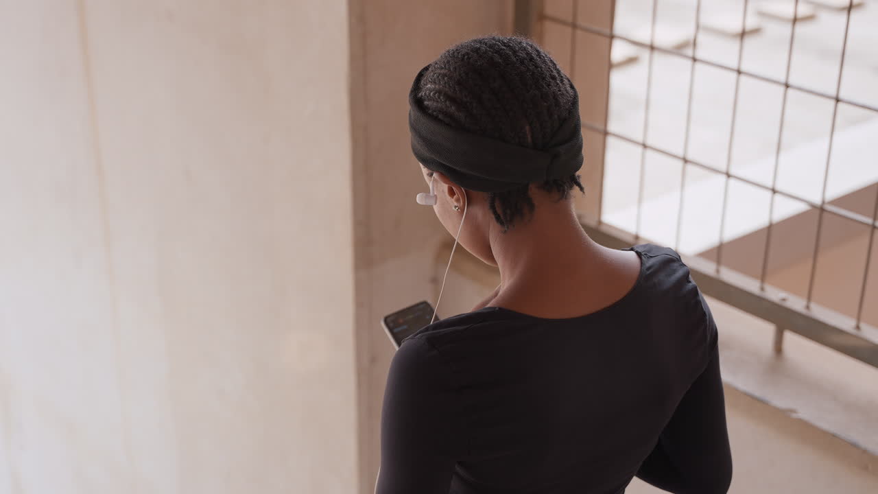 young woman on balcony scrolling phone, pearl earring chain, checking calendar and emails, deliberate gestures, sunlight through grid window, urban building backdrop, professional focus
