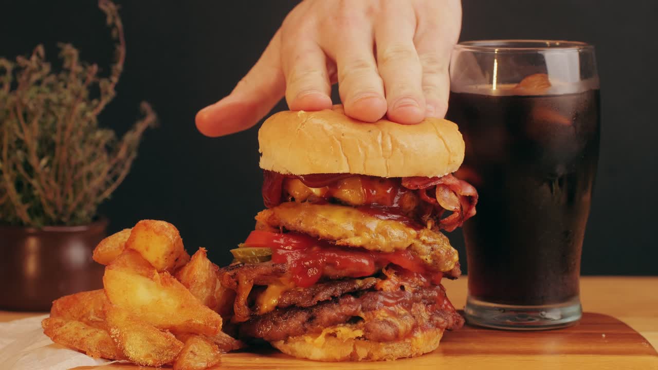 American fat smash burger with bacon slices and cheese on grill and country potatoes, with fresh ice coke close-up . Beef or pork cutlet smashing by burger press. The chef in kitchen of the restaurant making cutlets for burgers - smash burger beefsteak. Fast and street food concept.