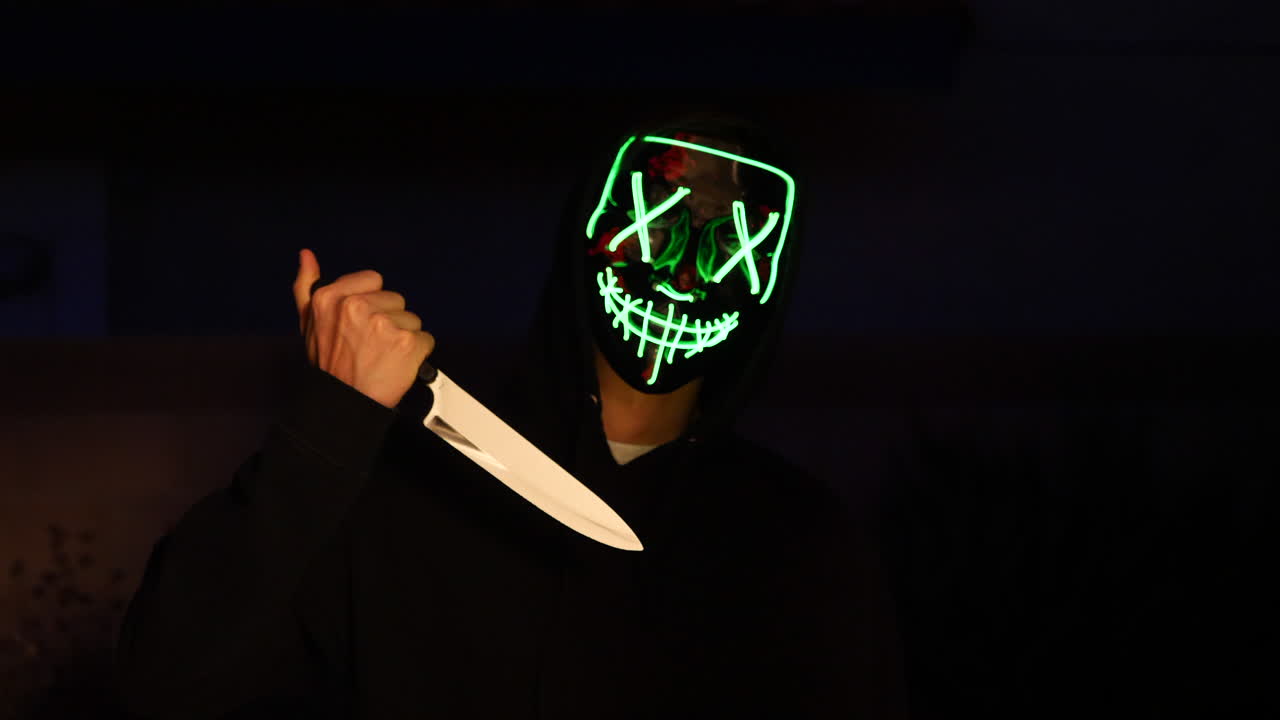 un asesino slasher aterrador con una máscara genérica anónima de terror de halloween tirando de un cuchillo a su víctima de asesinato