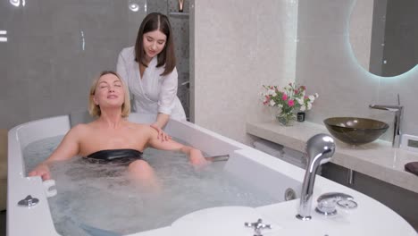 relaxed, beautiful woman lying in a hot tub in a spa salon. a beautician gives a health massage to a client.