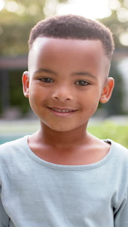 vertical video portrait of happy african american boy smiling in sunny garden, in slow motion