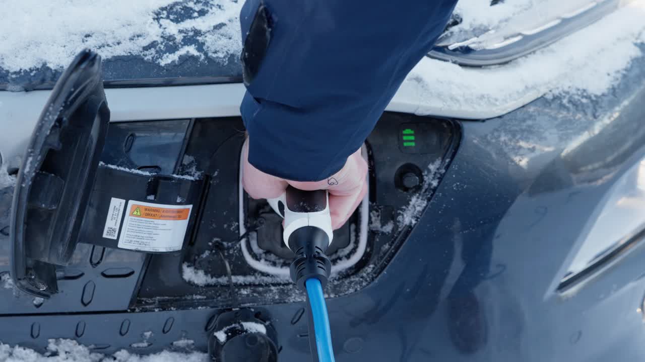Closeup of an EV charging hatch being opened, cable plugged in, and charging started in snowy and cold winter conditions