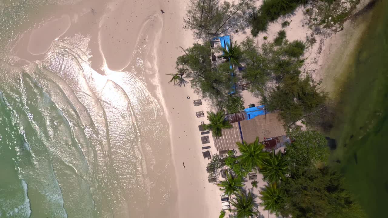 tropical Hut on white sand beach meeting calm turquoise water in Koh Rong island, Cambodia. Majestic aerial view flight vertical bird's eye view drone
