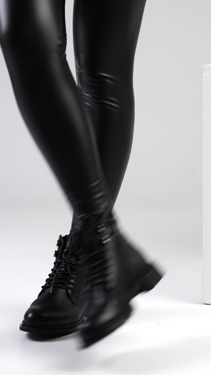 Female legs wearing black leather pants and boots. Stylish footwear concept. Model posing in white studio near white cube. Vertical video